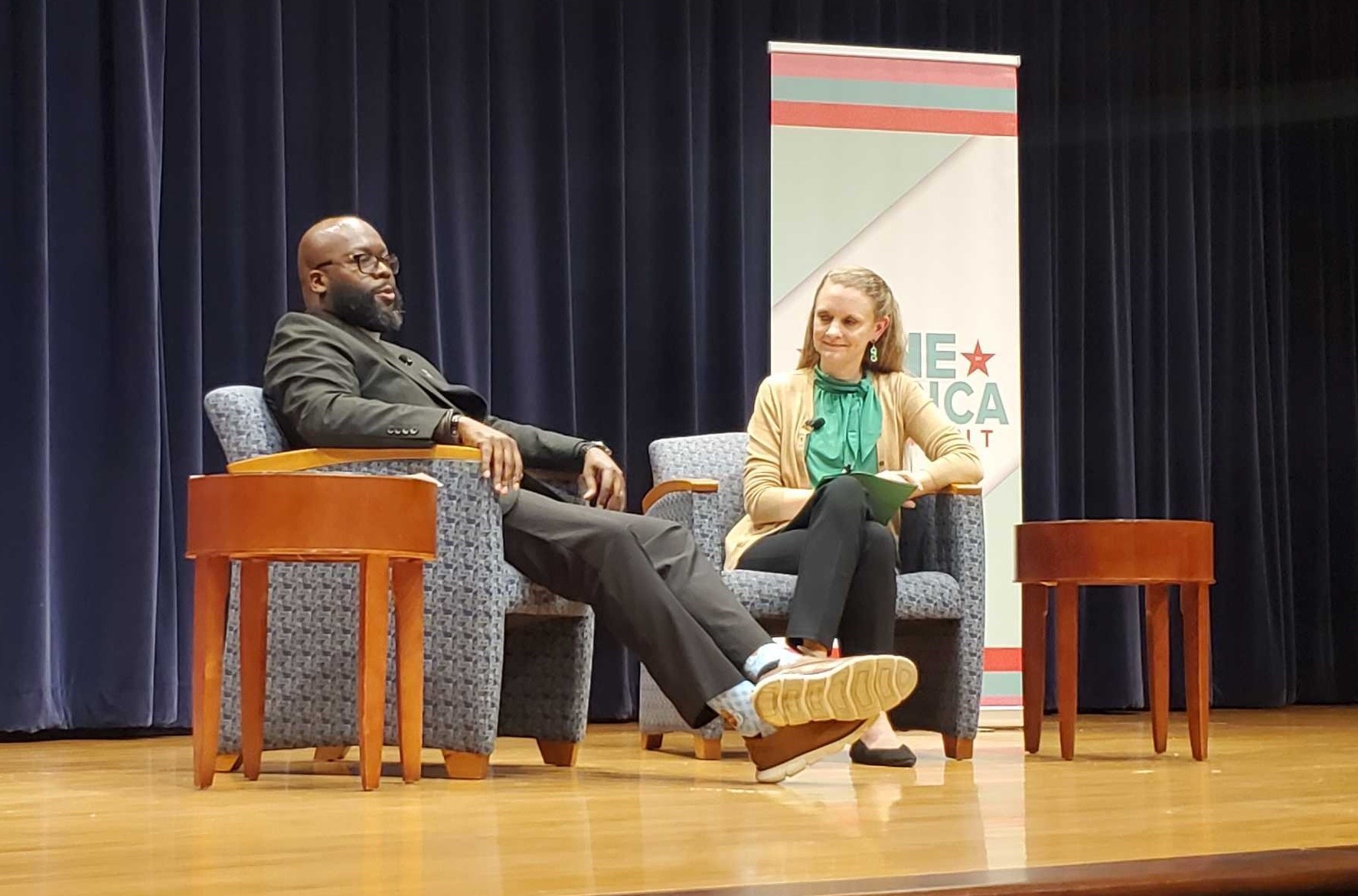 Two people on a stage in chairs having a conversation